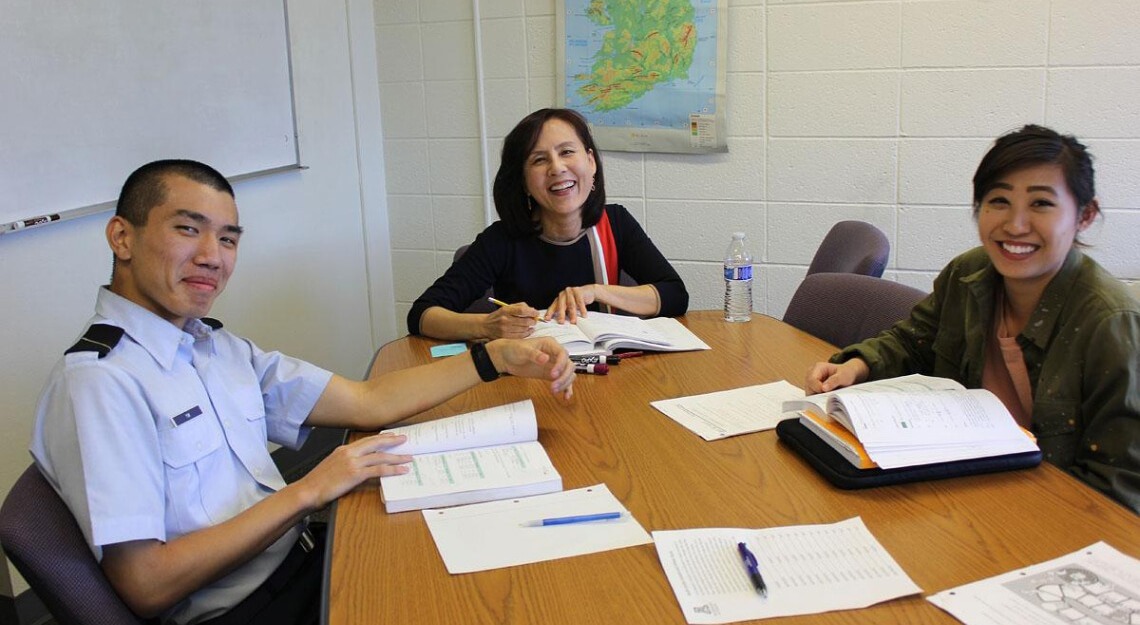 Professor sitting at a classroom table with Korean students.